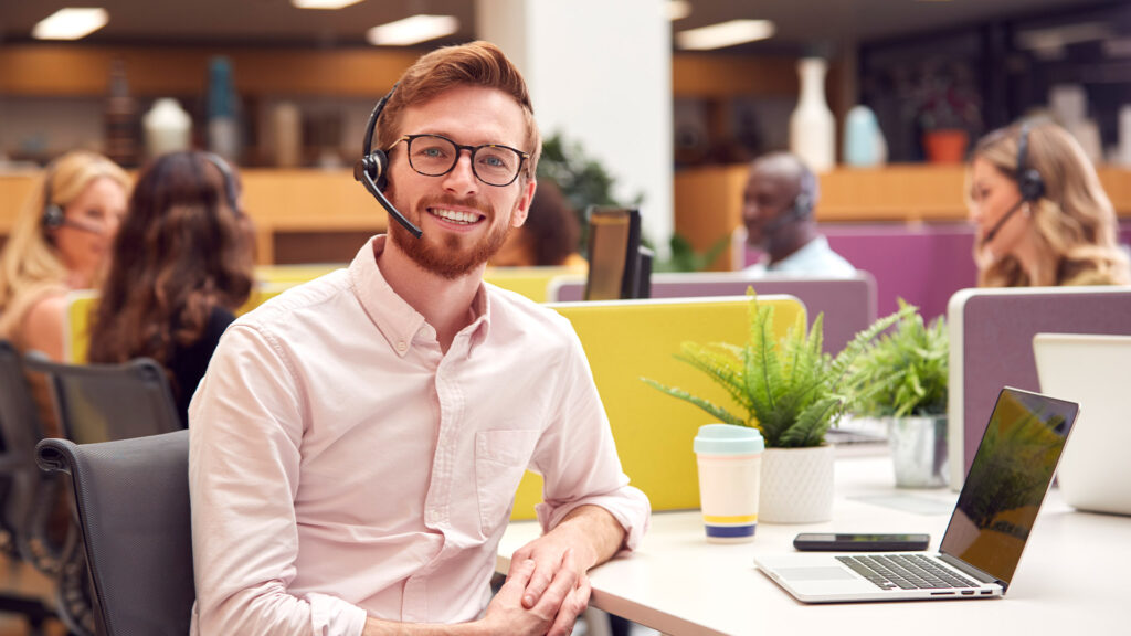 Portrait of a man wearing headset and talking to a caller in customer services centre